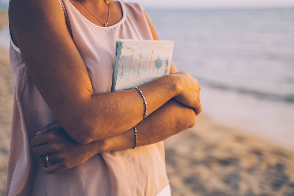 Close-up of a woman holding a notebook at the beach, creating a peaceful moment.