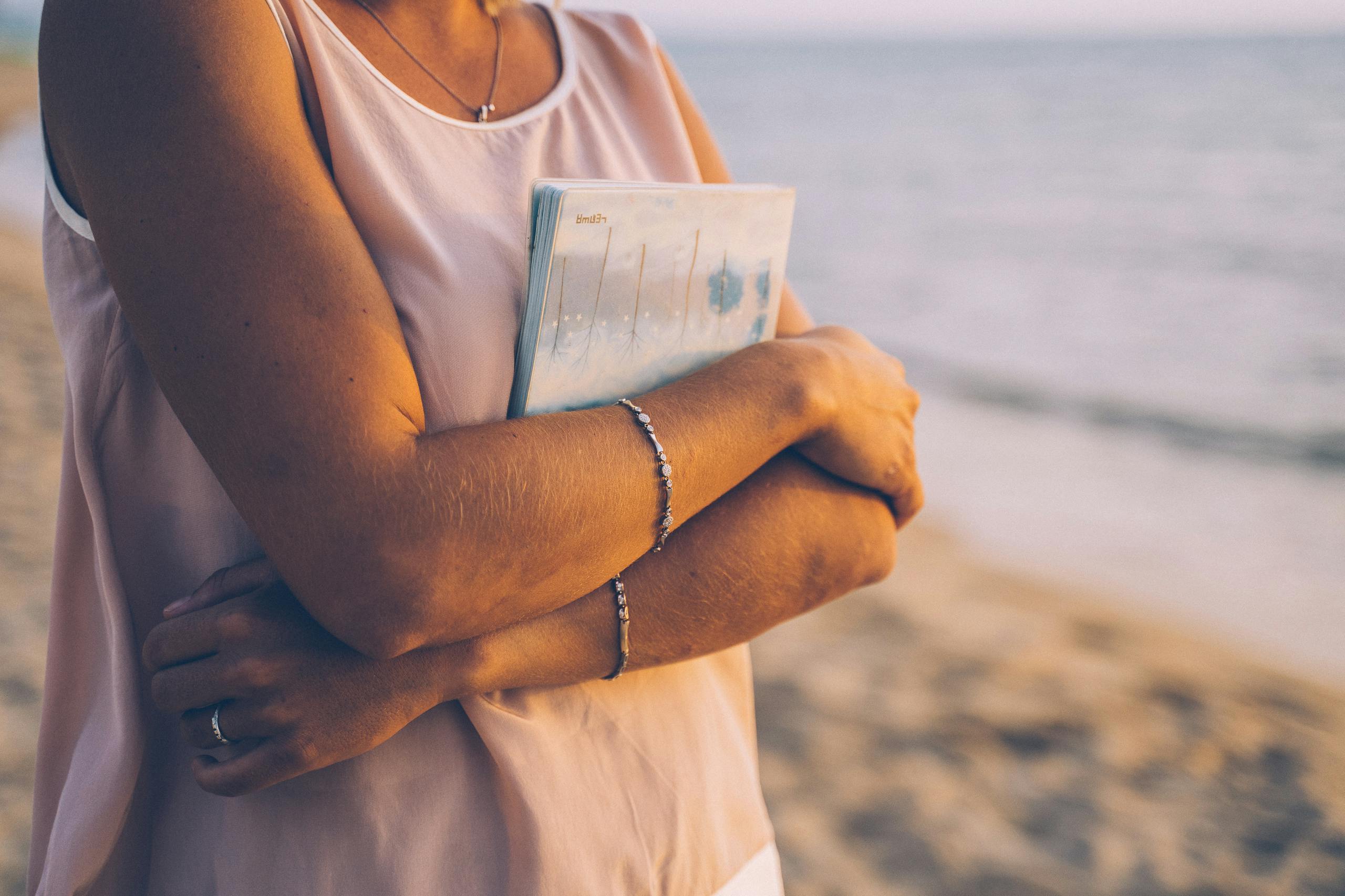 Close-up of a woman holding a notebook at the beach, creating a peaceful moment.